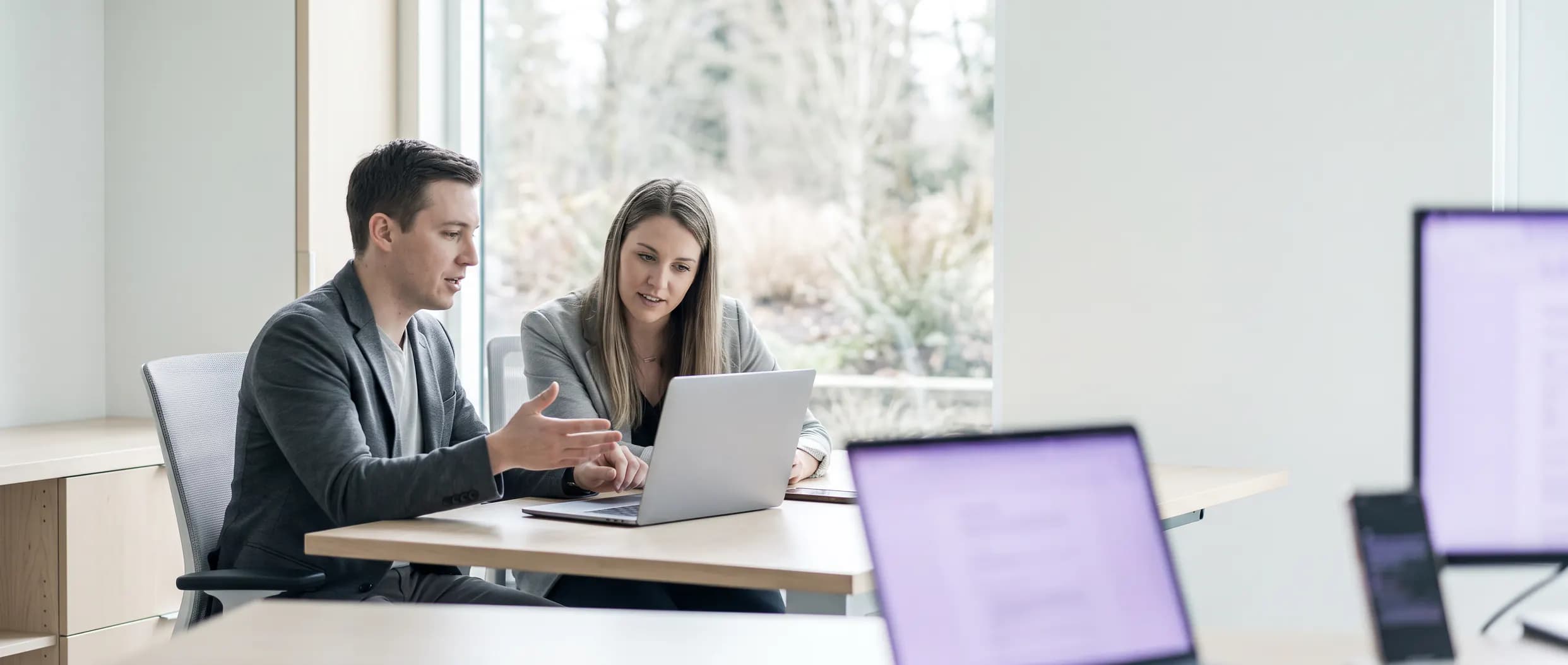 Two marketers side by side at a laptop, talking through which pages a site's traffic is actually landing on.