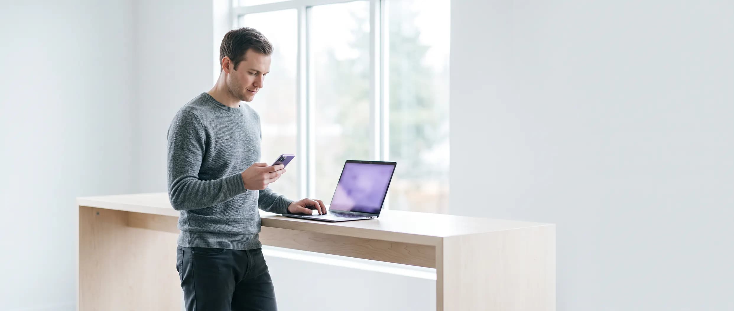 A business owner at a standing desk checking an answer on their phone, laptop open beside them.
