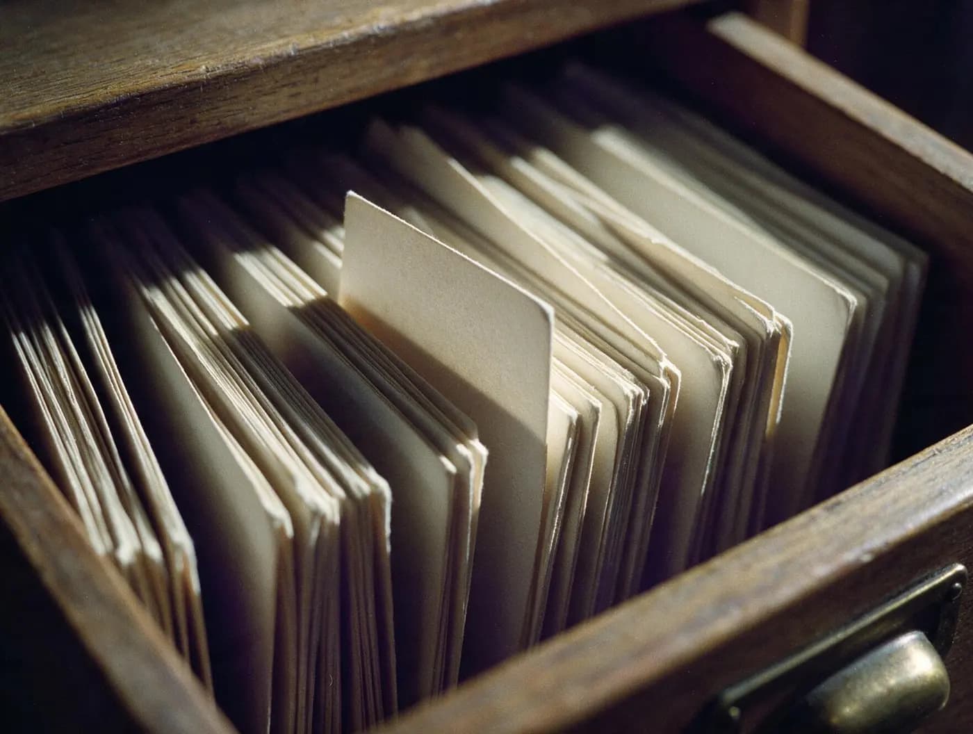 An open library card-catalogue drawer packed with index cards, one card raised proud of the rest and catching the light.